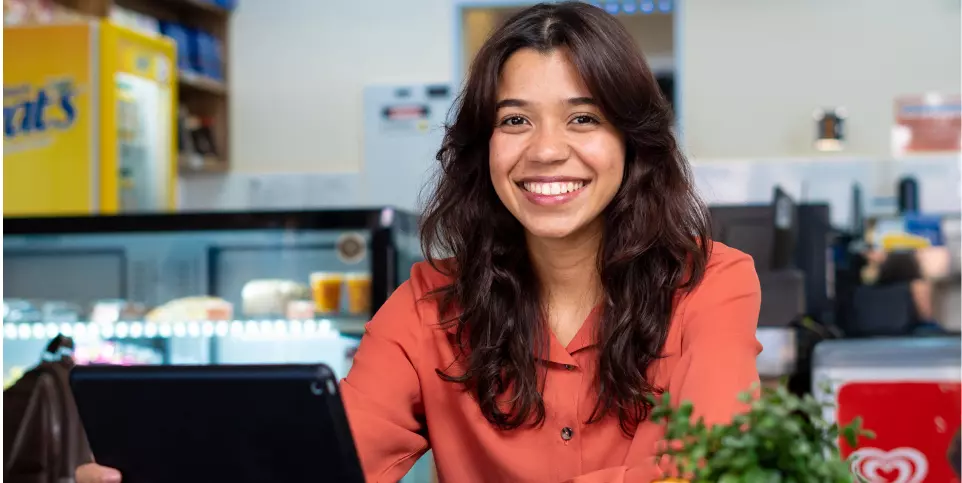 Mocça em uma mesa de cantina mexendo no computador e sorrindo